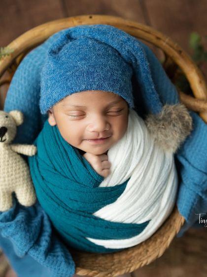 This little one is all smiles while cuddling his teddy bear. The textures of the knit hat, soft wrap, and wicker basket come together beautifully in this shot.