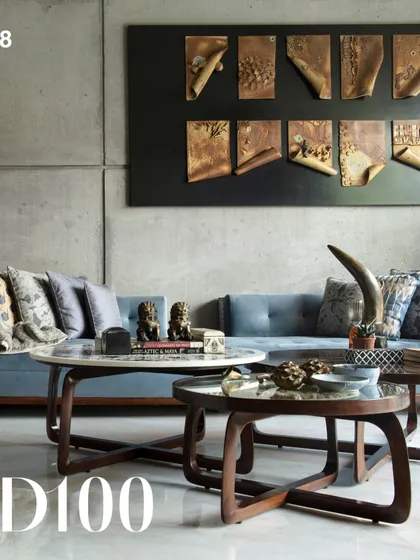 A living room from the Guha Residence, an AD100 project. This space showcases our custom-designed coffee tables and a comfortable blue sofa set against a board-formed concrete wall, balanced by intricate wall art.