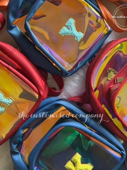 A collection of our custom swim bags for kids, shown in various colors like red and blue. The iridescent material and personalized initials make them a fun and practical accessory for pool days.