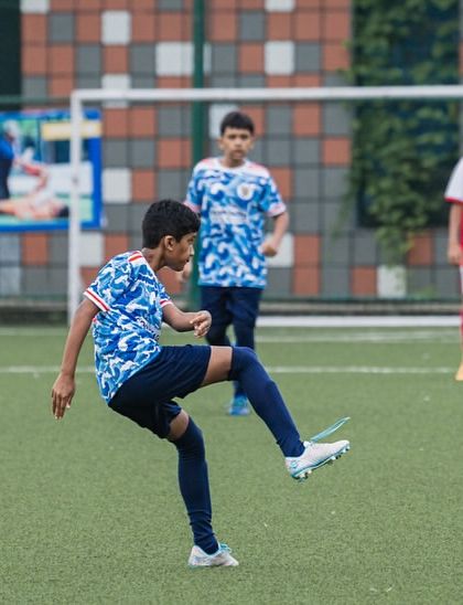 A player in our blue wave jersey controls the ball during a match. Our training focuses heavily on ball control and composure under pressure.