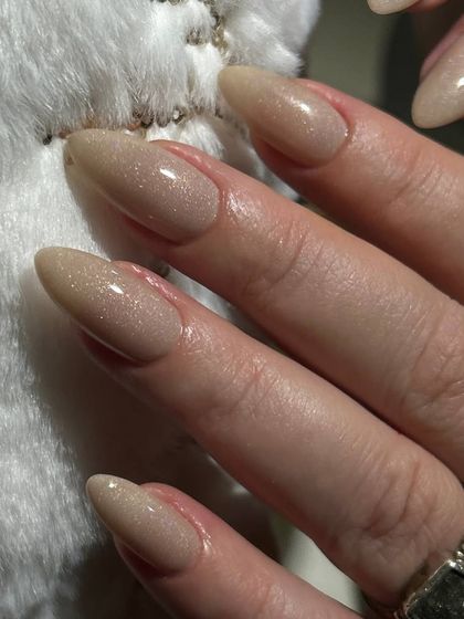 A subtle and elegant shimmery nude polish on long, almond-shaped nails. The light-reflecting particles give a beautiful, healthy glow.