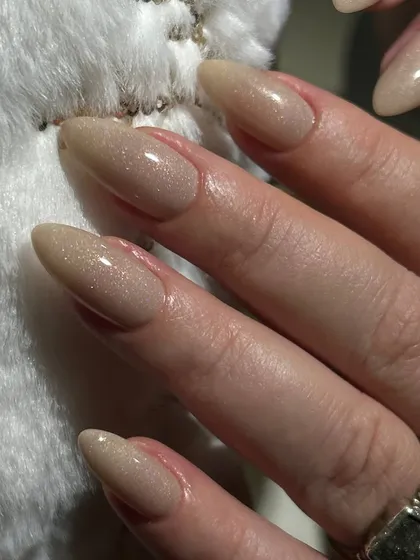 A subtle and elegant shimmery nude polish on long, almond-shaped nails. The light-reflecting particles give a beautiful, healthy glow.