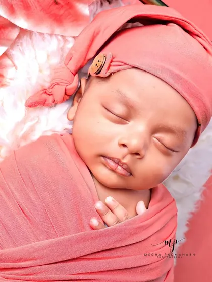 A close-up of a sleeping baby in a peach-colored wrap and hat.