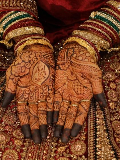 This bride's hands, adorned with her partner's name, look stunning against her rich red bridal attire. The dark stain makes the personalized detail stand out beautifully.