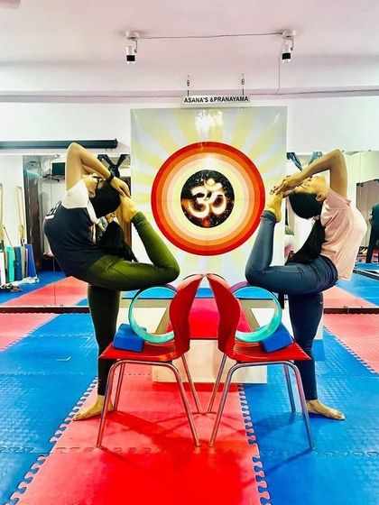 A creative use of props. Students perform Poorna Natarajasana (Full Lord of the Dance Pose) with the support of a chair and wheel to achieve the full expression.