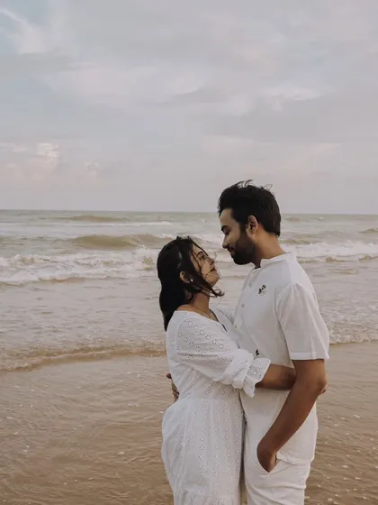 A classic romantic portrait on the beach. The couple, dressed in white, share a loving gaze with the endless ocean behind them, creating a timeless and serene image.