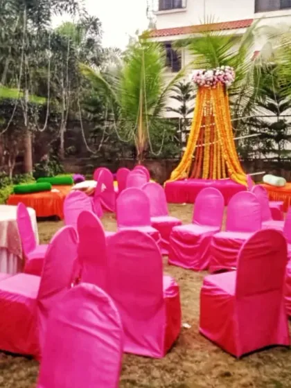 An outdoor Haldi function setup with bright pink chair covers and a simple, elegant seating area decorated with marigold garlands.