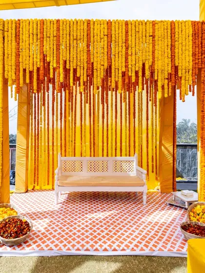 A traditional Haldi setup with a backdrop of marigold flower strings, showcasing our versatility in creating classic and timeless looks.
