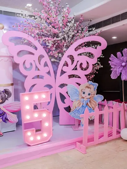 A closer look at the details of the Fairy Wonderland theme, showcasing the large, pink butterfly wing cutout, a light-up number '5', and adorable fairy character standees.