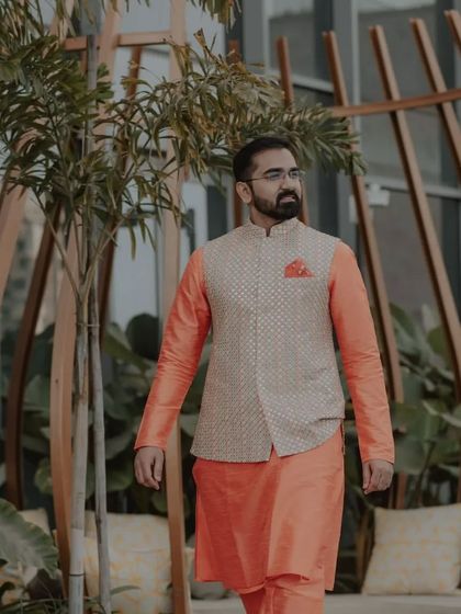 An orange silk kurta paired with an embroidered bandi jacket. The pocket square adds a final touch of polish to this vibrant pre-wedding outfit.