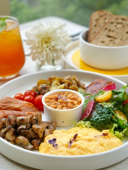 A complete breakfast plate with scrambled eggs, sausages, bacon, baked beans, and sautéed mushrooms. It's the perfect way to fuel up for the day ahead.