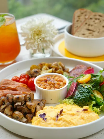 A complete breakfast plate with scrambled eggs, sausages, bacon, baked beans, and sautéed mushrooms. It's the perfect way to fuel up for the day ahead.