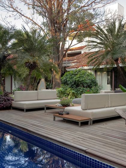 A modern poolside deck with minimalist outdoor sofas. The design is clean and uncluttered, allowing the reflections of the surrounding trees in the water to become a key feature of the space.