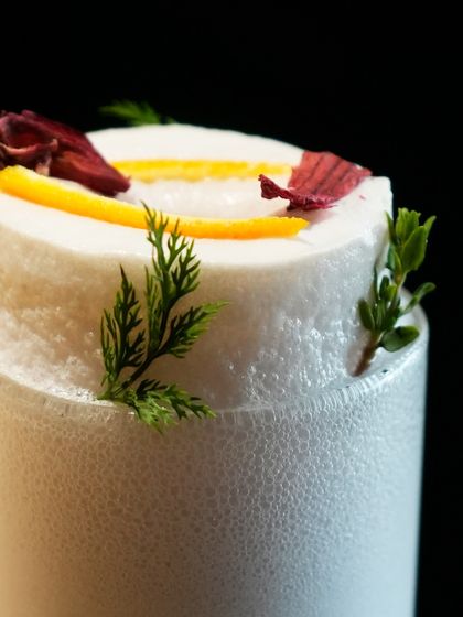 A close-up of the delicate foam and herbal garnish on our Ramos Gin Fizz, a cocktail that requires patience and precision to perfect.