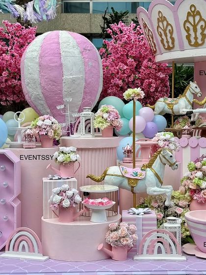 A whimsical pastel carousel theme for a 3rd birthday party. The decor features a large carousel top, miniature horses, a hot air balloon prop, and soft pastel colors for a sweet and playful vibe.