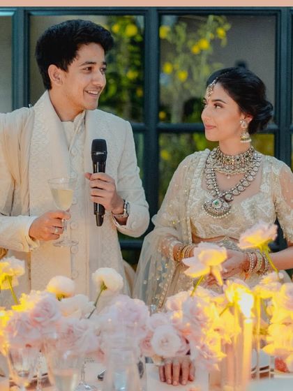 A candid shot of the couple giving a speech at their reception dinner, framed by soft flowers and candlelight.