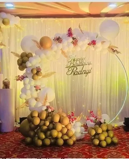 An elegant and sophisticated first birthday setup. This decoration uses a soft color palette of white and olive green, with a circular frame, a light-up number '1', and delicate floral accents.