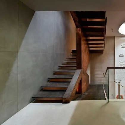 Another view of the staircase and temple, showing the interplay of light, shadow, and material. The raw concrete-finish walls provide a neutral backdrop for the warmth of the wood and the intricacy of the stone carving.