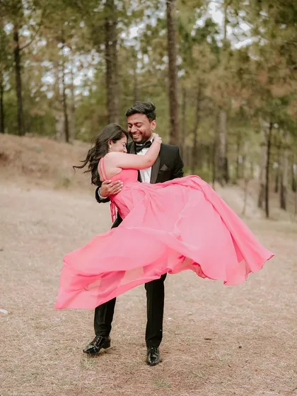 A romantic moment from a pre-wedding shoot in the hills of Himachal. The groom lifts his bride, her pink gown flowing, surrounded by the serene beauty of a pine forest.