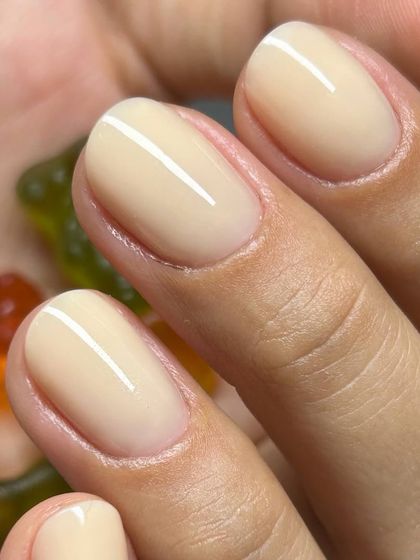 A perfect, creamy nude manicure. This photo, with gummy bears in hand, shows the playful side of a classic, beautifully executed nail look.