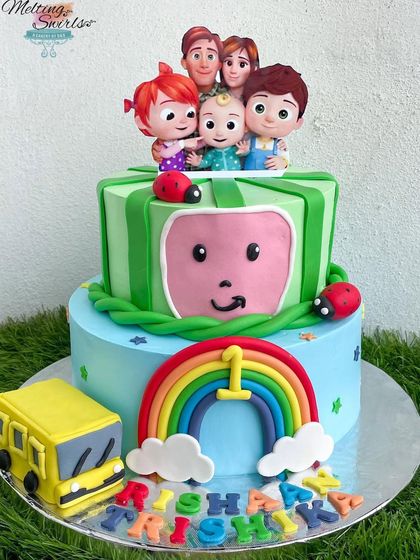 This two-tier Cocomelon cake is one of our most popular designs for first birthdays. It features the iconic watermelon logo, a school bus, and the whole Cocomelon family, all made with fondant on a whipped cream cake.