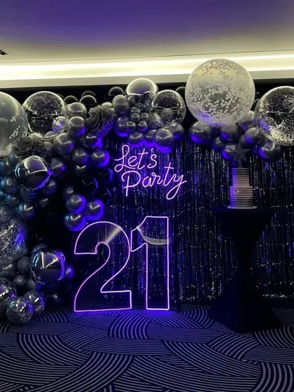 For this 21st birthday, we went for a chic and modern party vibe. The centerpiece is the glowing neon signage, including the age and a 'Let's Party' sign. I paired it with a dramatic backdrop of a silver tinsel curtain and a cascade of chrome and confetti balloons for a truly stylish celebration.