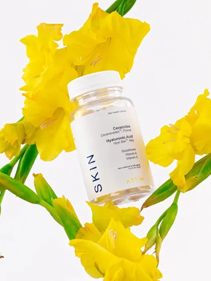 A creative shot of a skin supplement floating among fresh yellow flowers. This composition visually connects the product to natural ingredients and a sense of vitality and beauty.