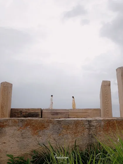 A symmetrical wide shot of a couple facing each other on a stone wall, framed by pillars.