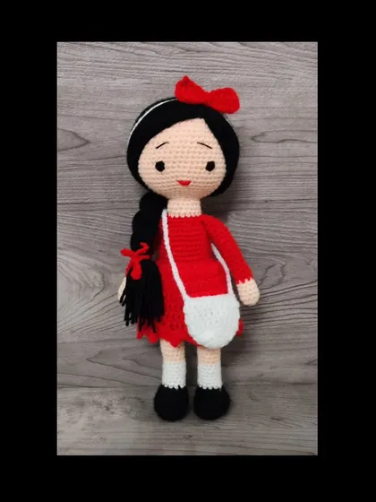 A sweet doll in a red dress with a white bag. Her long black hair is in a single braid.