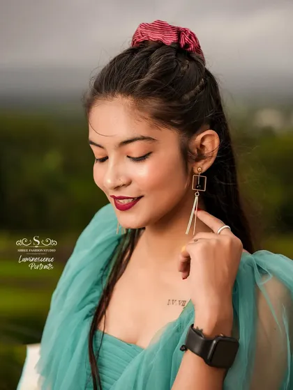 A close-up portrait capturing the model's gentle smile and elegant style, with her teal dress and modern earrings.