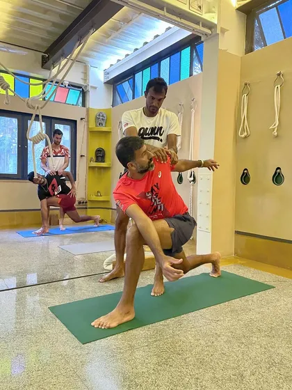 A hands-on adjustment for a tennis player in a twisting lunge. These adjustments help the athlete understand the rotation in the spine and the opening in the chest, which is crucial for sports involving rotational movements.