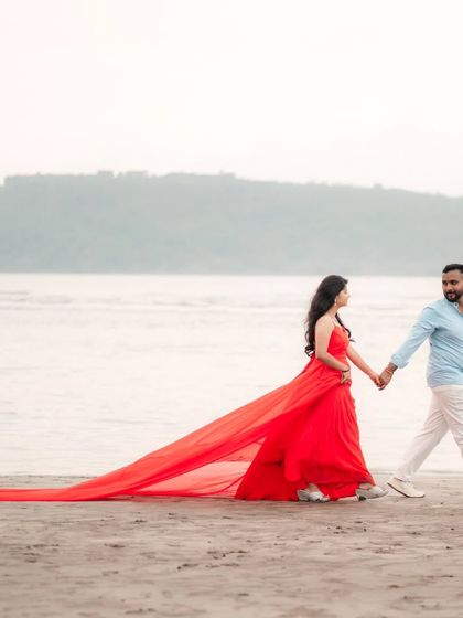 Hand in hand, walking along the shore. The long red trail of the gown creates a beautiful line in this serene pre-wedding beach photo.