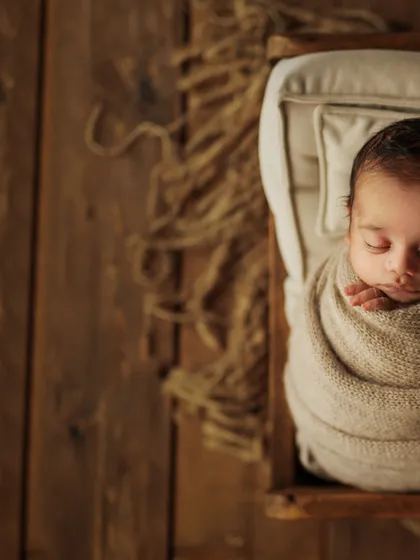A wider perspective of this rustic setup, showing the beautiful wooden textures and jute rug that complement the simple, earthy wrap. This style creates a warm and timeless feel for your baby's first portraits.