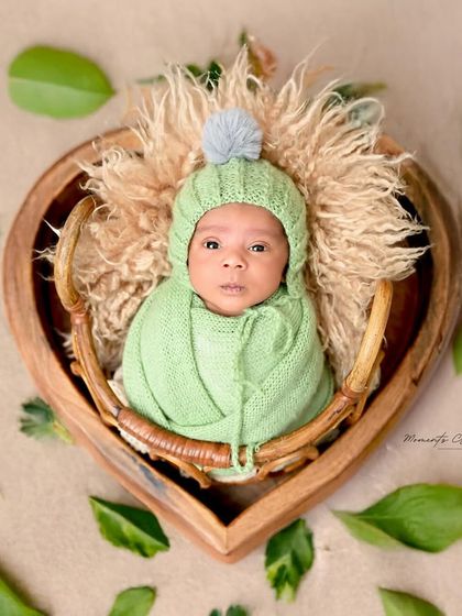 Wide-eyed and wonderful. This alert newborn looks directly into the camera from his cozy, heart-shaped basket, showing a glimpse of his curious little personality.