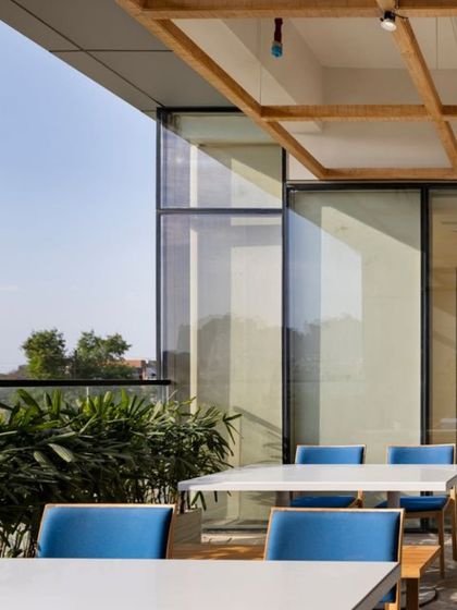 An outdoor terrace at the Godrej Woods Clubhouse provides a casual setting for dining or relaxing. The design prioritizes natural materials and views, blurring the line between inside and out.