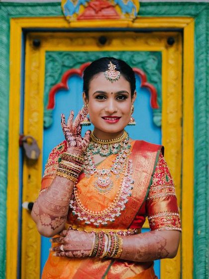A beautiful bride displaying her henna-stained hands against a colorful backdrop. The deep color of the mehndi is a key part of the traditional bridal look.