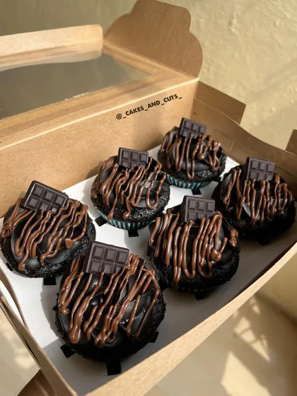 A box of rich, dark chocolate cupcakes with a chocolate drizzle and a small chocolate bar on top.
