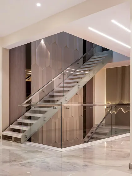 A striking modern staircase with a glass railing, set against a wall of geometric, three-dimensional panels. The design is both a functional element and a sculptural work of art.