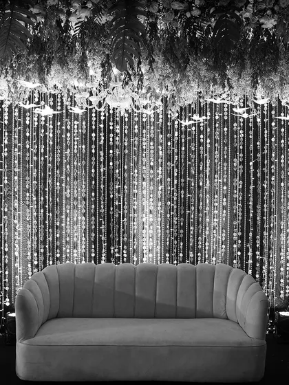 This black and white photograph highlights the timeless texture and form of our stage design. The contrast emphasizes the shimmering bead curtain, the lush floral ceiling, and the elegant silhouette of the velvet sofa.