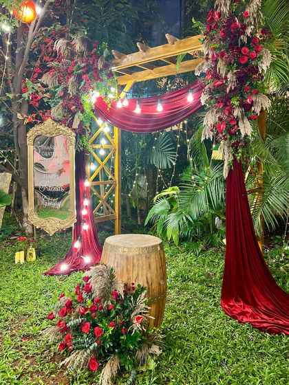 Another angle of the Friendsgiving setup, showing the lush greenery of the garden blending perfectly with the deep red floral arrangements and rustic decor elements.