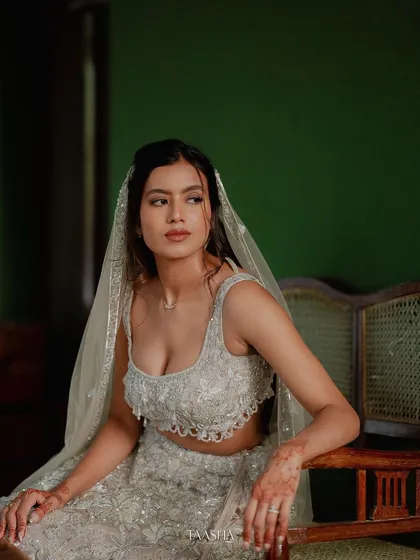 A bride in a modern silver lehenga, seated, her long veil creating a dramatic and beautiful effect.
