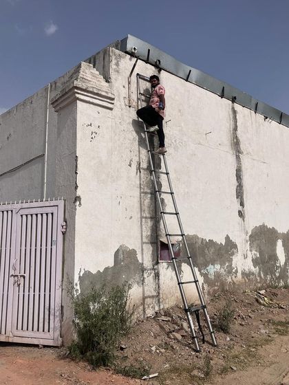 No height is too much for my team. Here, a technician is climbing a high ladder to install a camera on the exterior of a large warehouse, ensuring no blind spots.