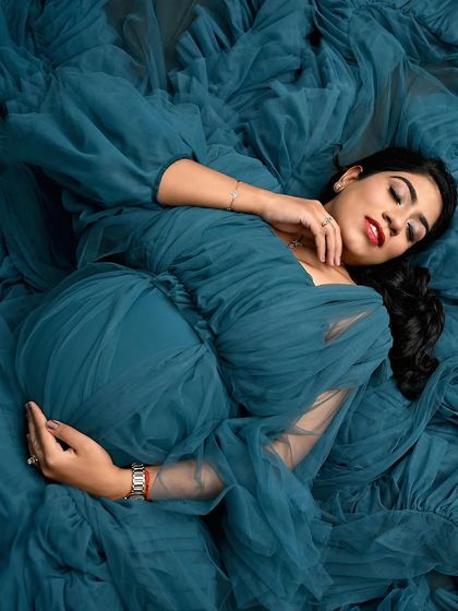 A serene and artistic top-down shot. Lying in a sea of blue tulle, this portrait focuses on the peaceful moment of connection between mother and baby.