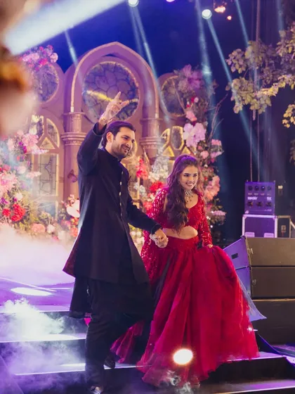 The couple shares a dance on stage, framed by the ornate, illuminated window backdrops and soft smoke effects.
