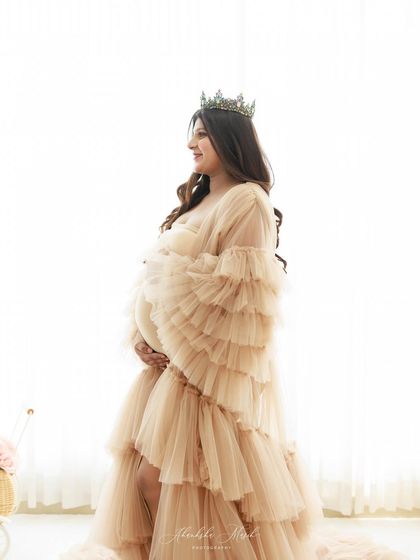 A high-key portrait where the mother-to-be, wearing a crown and a ruffled gown, is bathed in soft, bright light for an angelic feel.