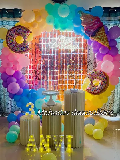 A sweet treats theme for a third birthday. This colorful setup includes a circular balloon arch, a shimmer backdrop, large donut and ice cream foil balloons, and a light-up number '3'.