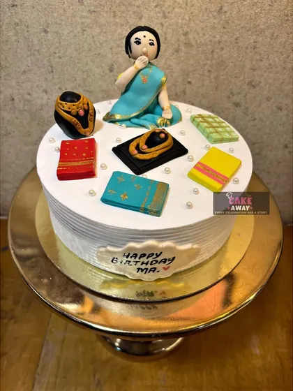 A thoughtful cake for a mother, featuring a fondant figurine of a woman in a saree surrounded by smaller edible sarees.
