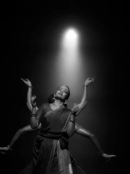 A black and white shot of a dancer reaching towards a single spotlight in 'Nagamandala'. This highlights the importance of lighting in guiding the audience's focus and creating dramatic tension.