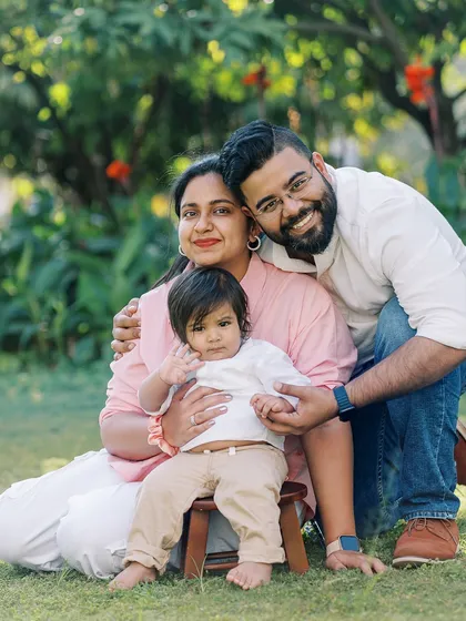 A happy family portrait in a lush green setting, celebrating their son's first birthday with a simple, natural feel.