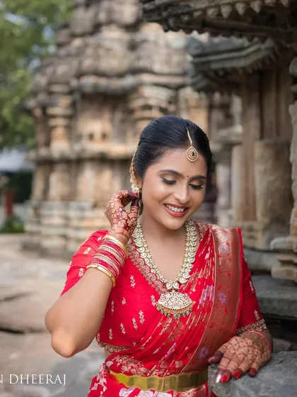 A bride in a vibrant red saree, posing against the backdrop of a historic temple. Her custom red blouse is adorned with delicate embroidery, perfect for a pre-wedding photoshoot.